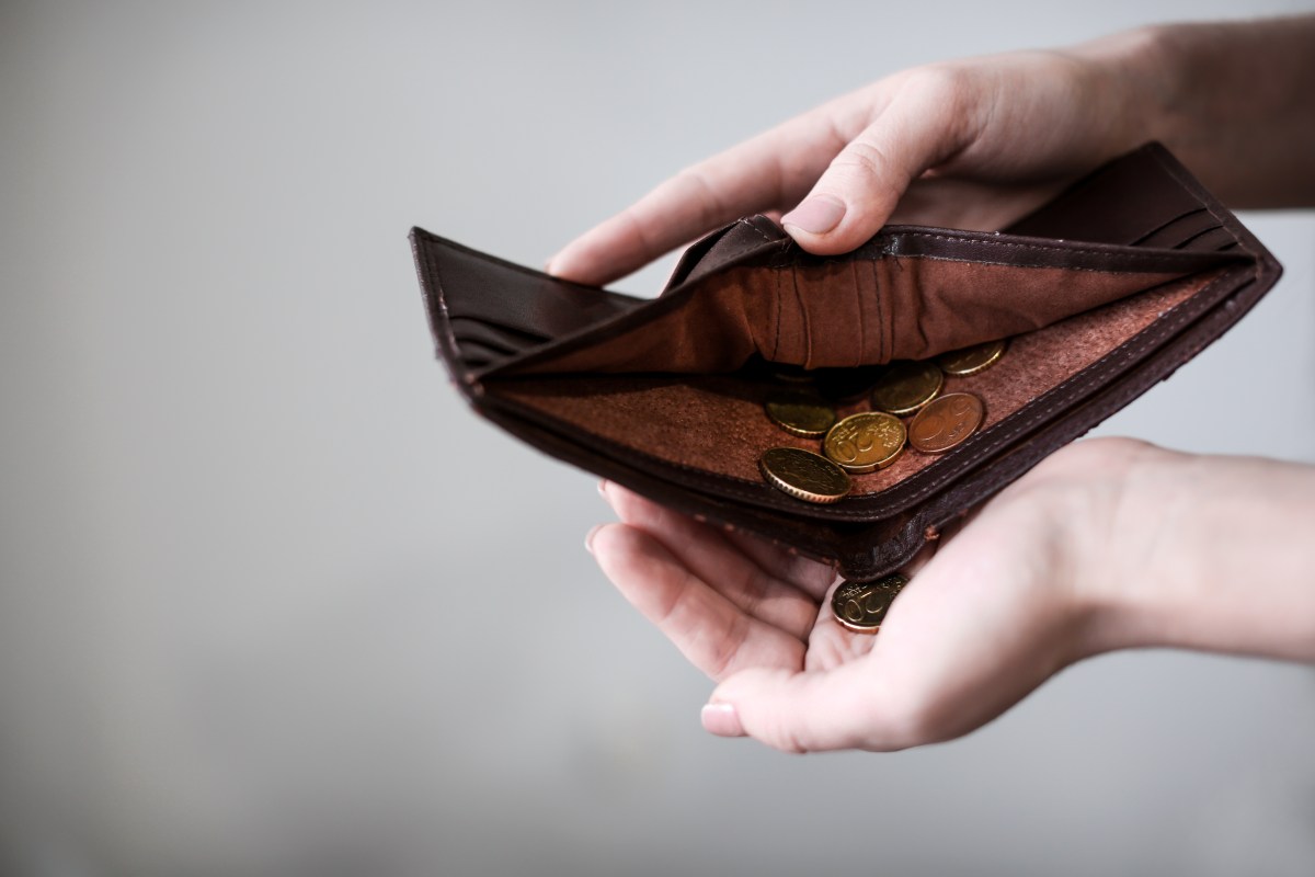 Eine Person hält ein Portemonnaie mit wenigen Münzen in der Hand.