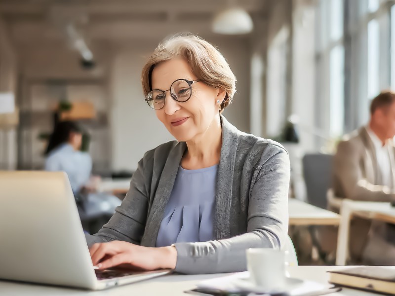 Eine Ã¤ltere Dame sitzt im BÃ¼ro am Computer.