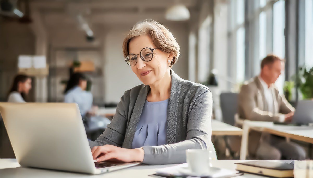 Eine Ã¤ltere Dame sitzt im BÃ¼ro am Computer.