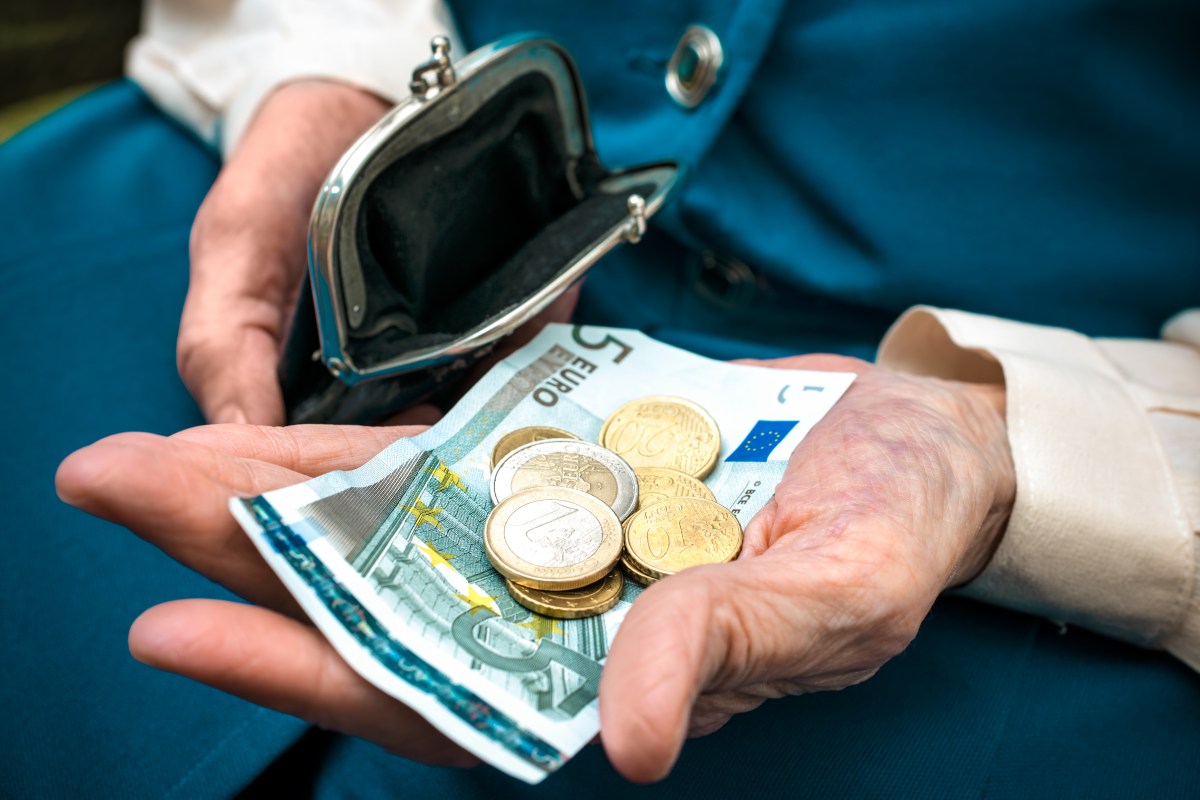 In einer Hand eines Senioren liegt ein Fünf-Euro-Schein und Münzen.