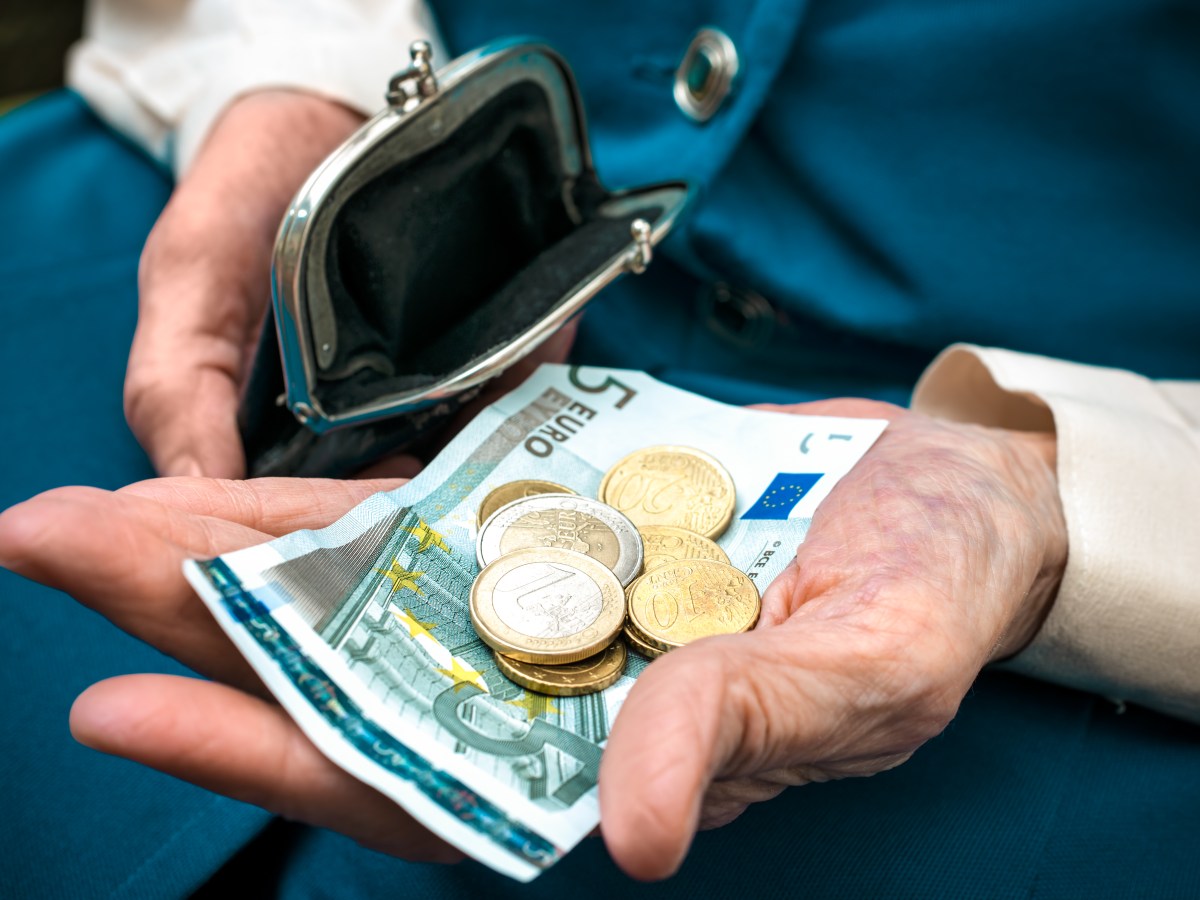 In einer Hand eines Senioren liegt ein Fünf-Euro-Schein und Münzen.