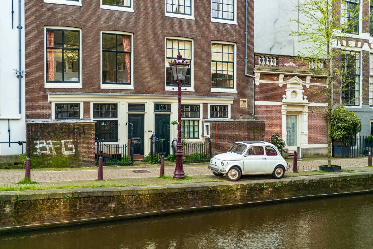 Ein kleines Auto steht am Kanal vor einem Haus in Amsterdam.