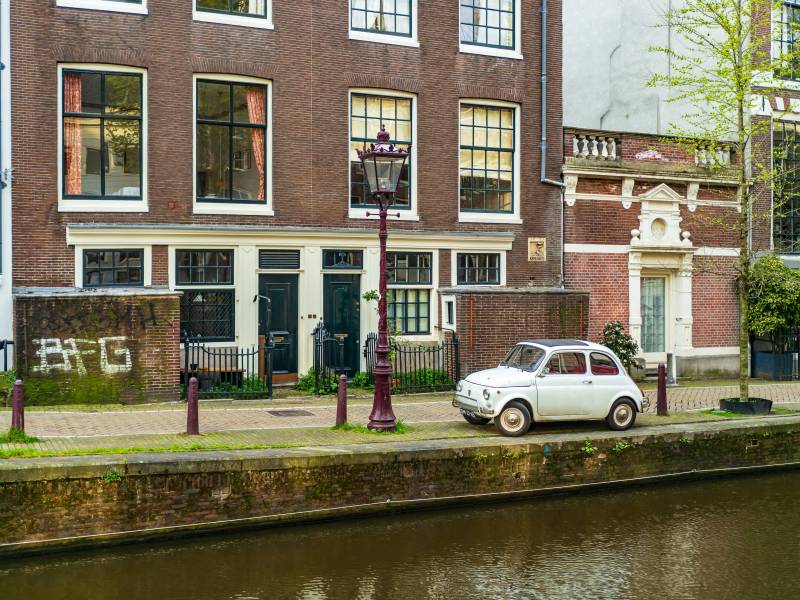Ein kleines Auto steht am Kanal vor einem Haus in Amsterdam.