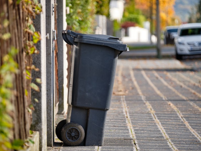 Eine schwarze MÃ¼lltonne steht am StraÃŸenrand.