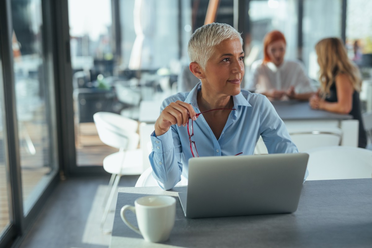 Eine Ã¤ltere Dame mit grauen Haare sitzt im BÃ¼ro vor ihrem Laptop.