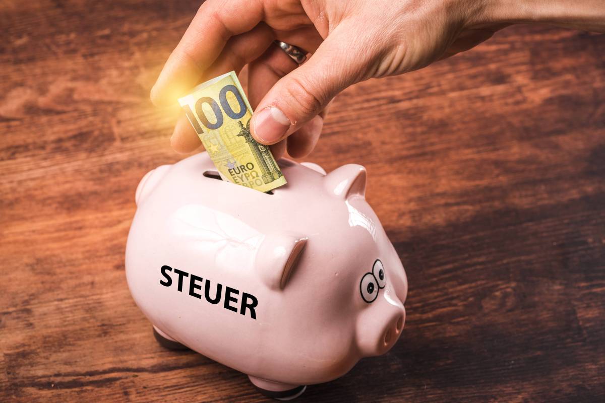 Eine Person wirft 100 Euro in ein Sparschwein mit der Aufschrift "Steuer".