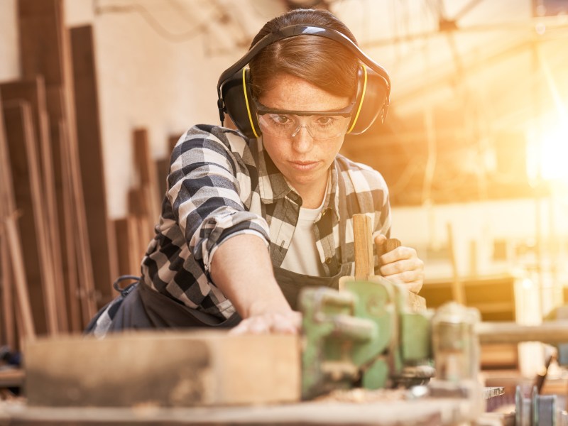 Eine junge Frau arbeitet in der Werkstatt. Sie sÃ¤gt Holz.