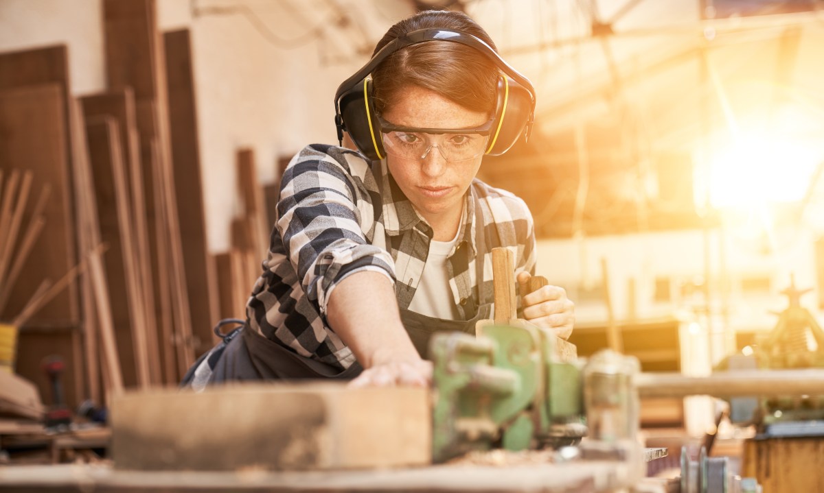 Eine junge Frau arbeitet in der Werkstatt. Sie sÃ¤gt Holz.