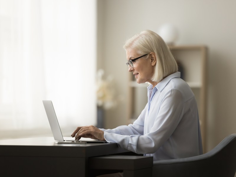 Eine Ã¤ltere Dame mit weiÃŸen Haaren sitzt vor dem Laptop und arbeitet.