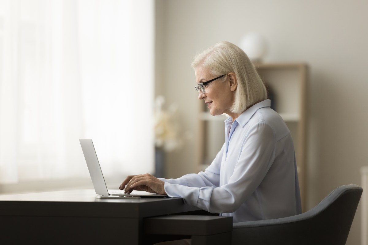 Eine Ã¤ltere Dame mit weiÃŸen Haaren sitzt vor dem Laptop und arbeitet.