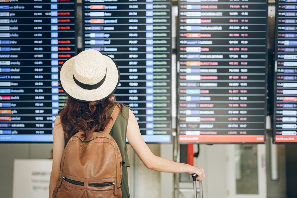 Frau checkt am Flughafen die Flugtafel