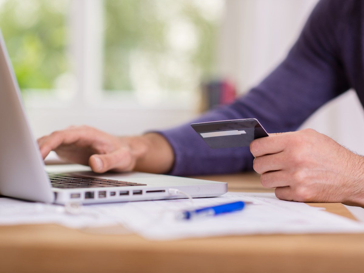 Eine Person sitzt am Laptop und hÃ¤lt eine Bankkarte in der Hand.