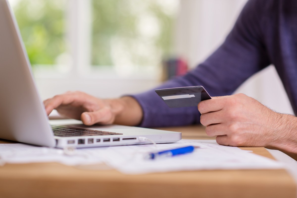 Eine Person sitzt am Laptop und hält eine Bankkarte in der Hand.