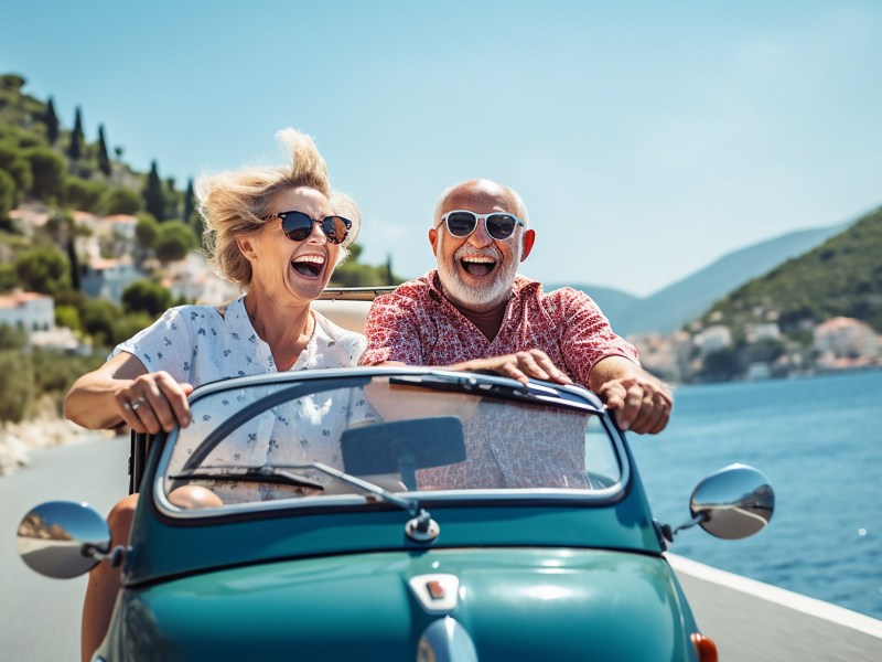 Ein Seniorenpaar sitzt im Cabrio und fÃ¤hrt an der KÃ¼ste entlang.