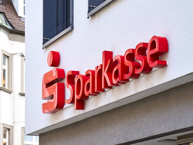 An einem Gebäude hängt das Logo und der Schriftzug der Sparkasse.