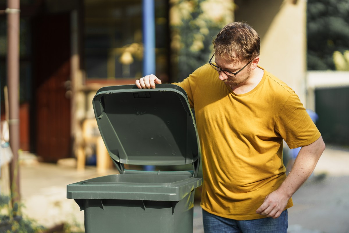 Eine Mann schaut in eine grÃ¼ne MÃ¼lltonne.