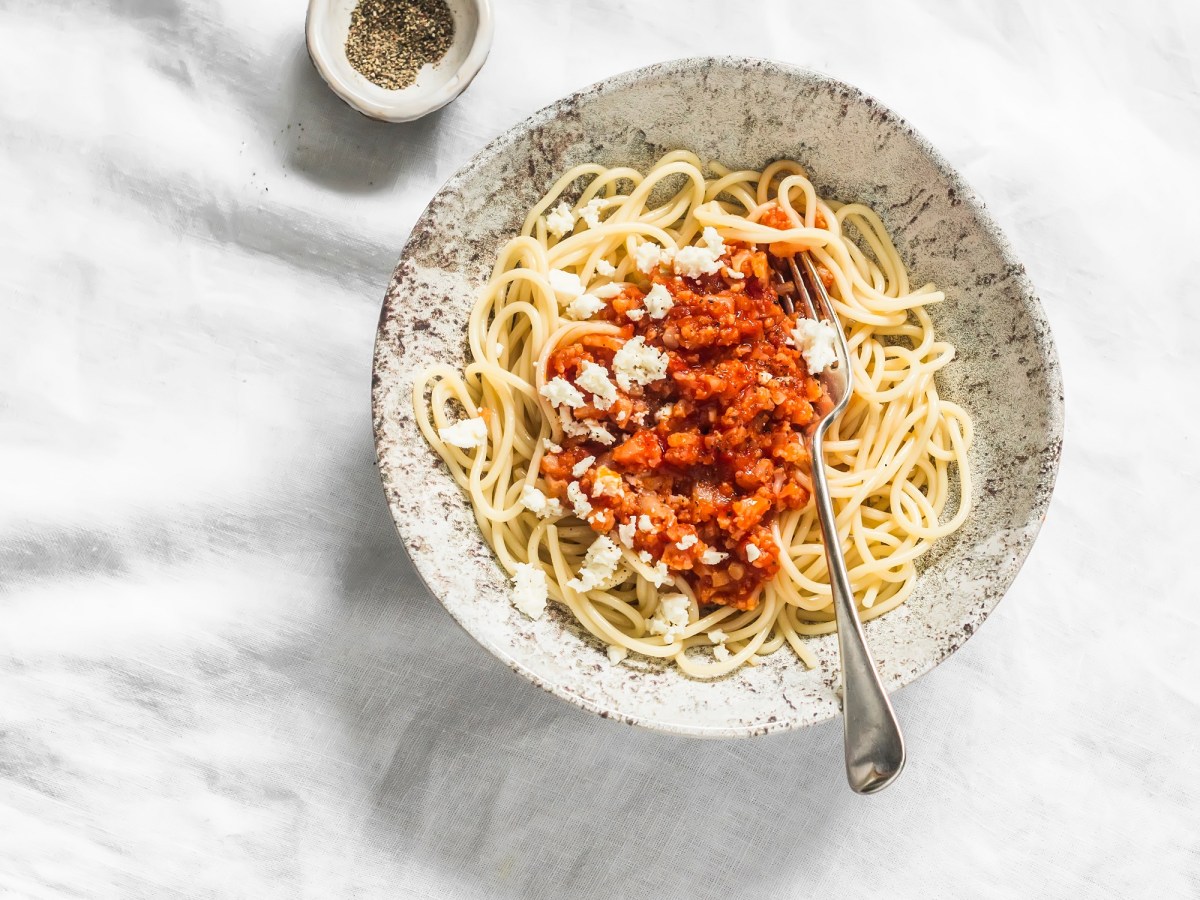 Teller mit Blumenkohl-Bolognese auf hellem Tischtuch.