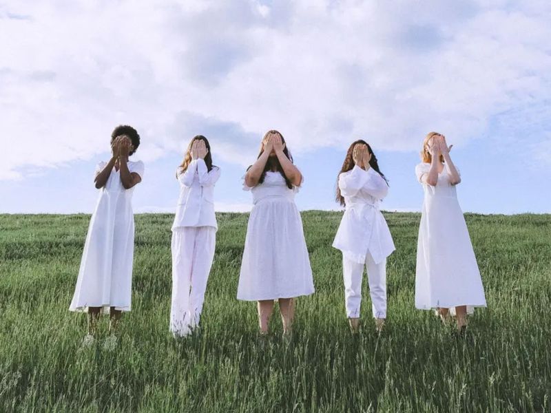 Embodiment: Frauen stehen auf einer Wiese und halten sich die HÃ¤nde vors Gesicht.