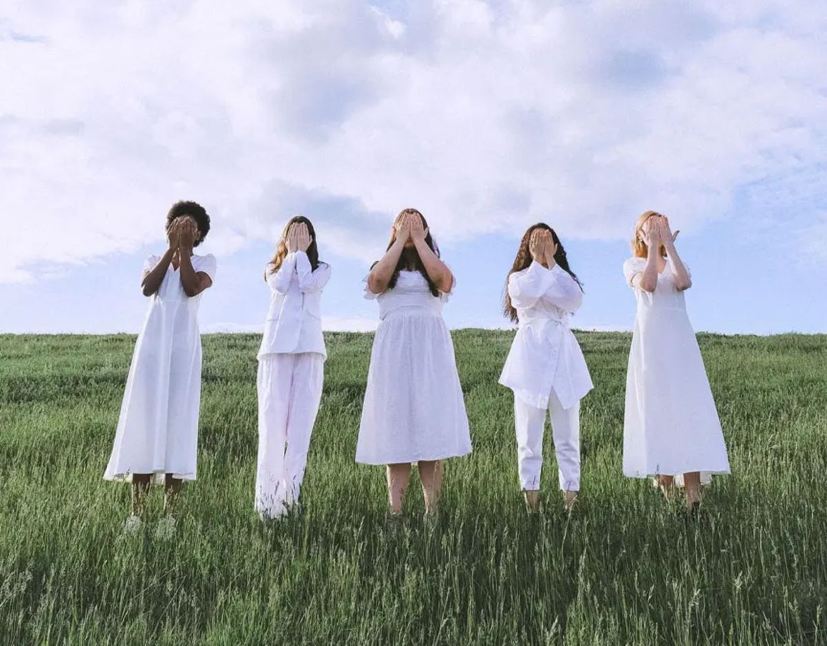 Embodiment: Frauen stehen auf einer Wiese und halten sich die HÃ¤nde vors Gesicht.