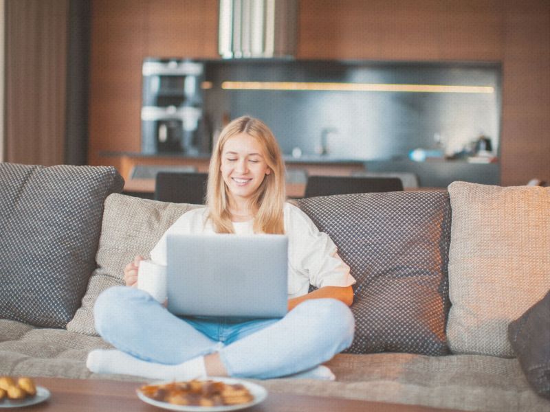 Eine junge Frau sitzt auf dem Sofa und schaut auf ihren Laptop.