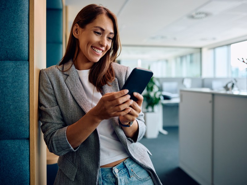 Eine Frau steht im Büro und schaut auf dem Handy.