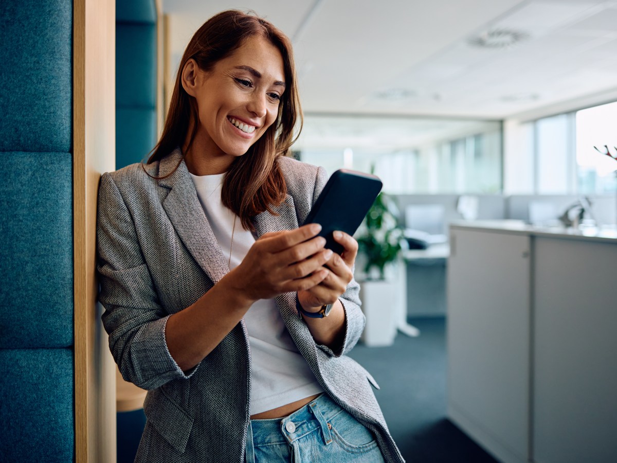 Eine Frau steht im BÃ¼ro und schaut auf dem Handy.