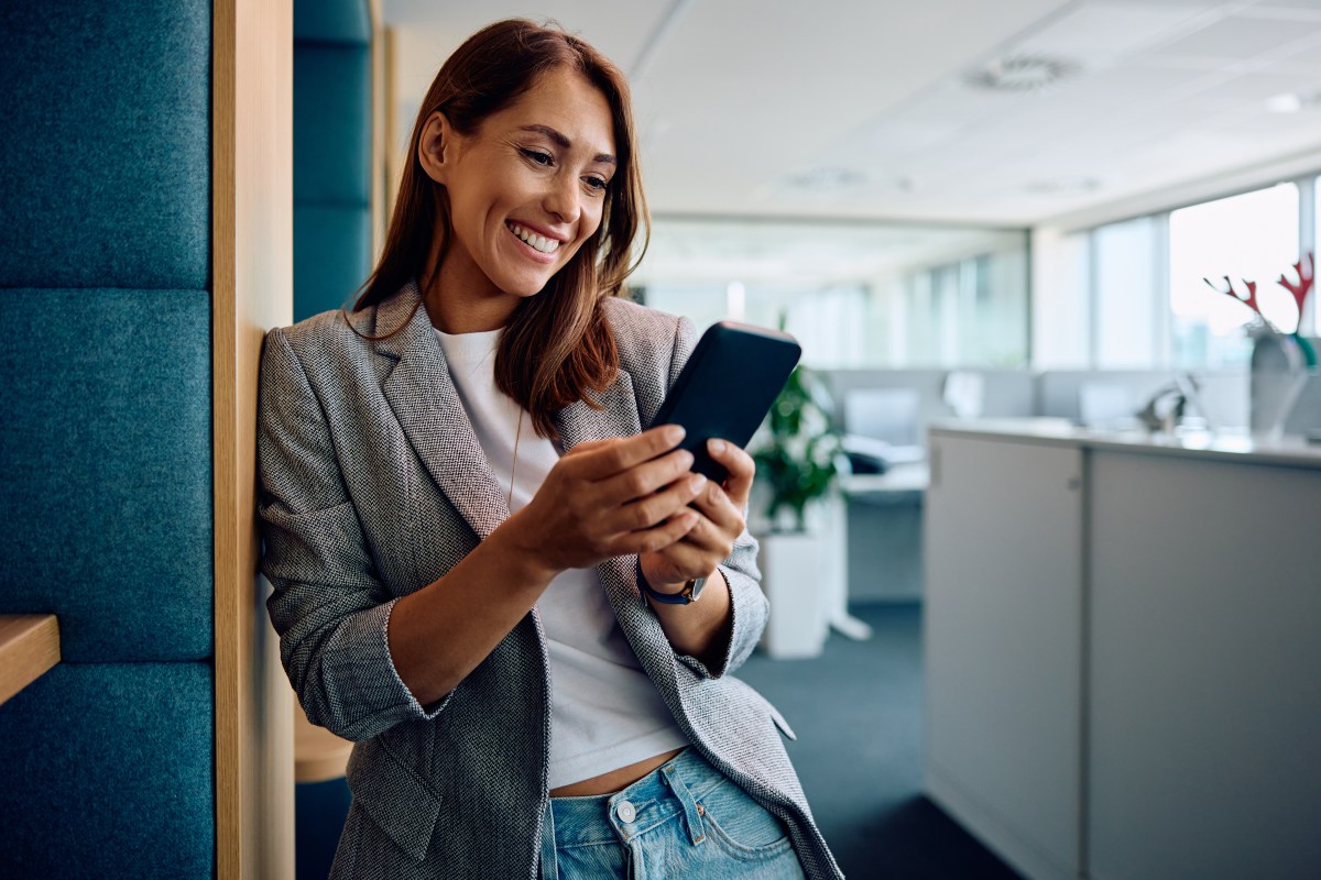 Eine Frau steht im Büro und schaut auf dem Handy.