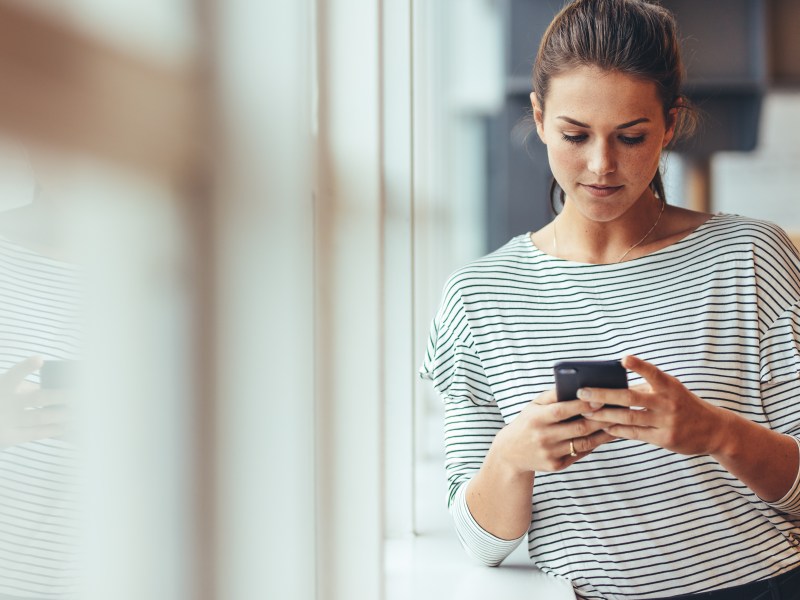 Eine Frau im gestreiften Shirt schaut auf ihr Handy.