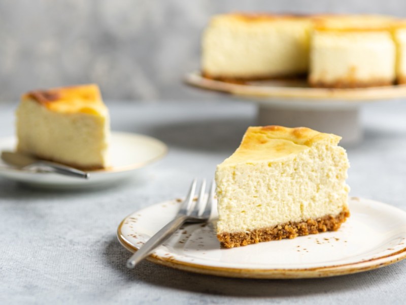 Zwei Stücke Käsekuchen mit Mascarpone auf zwei Tellern. Im Hintergrund ist der restliche Kuchen zu sehen.