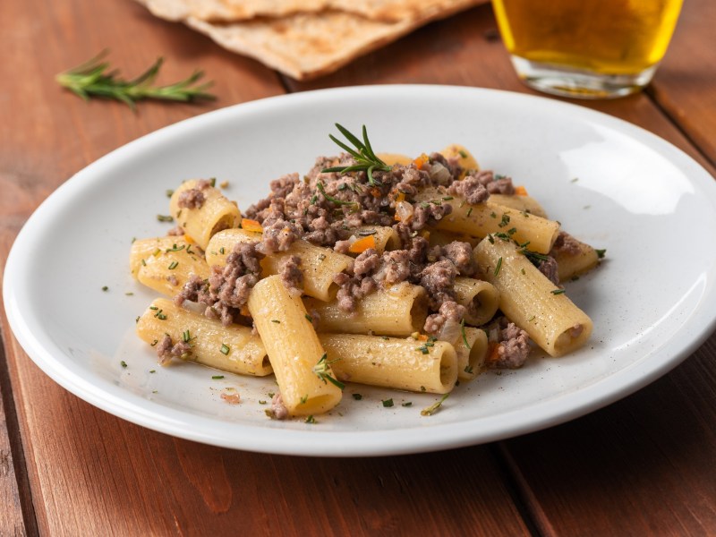 Rigatoni mit weiÃŸer Bolognese auf einem weiÃŸen Teller. Die Nudeln sind mit KrÃ¤utern dekoriert.