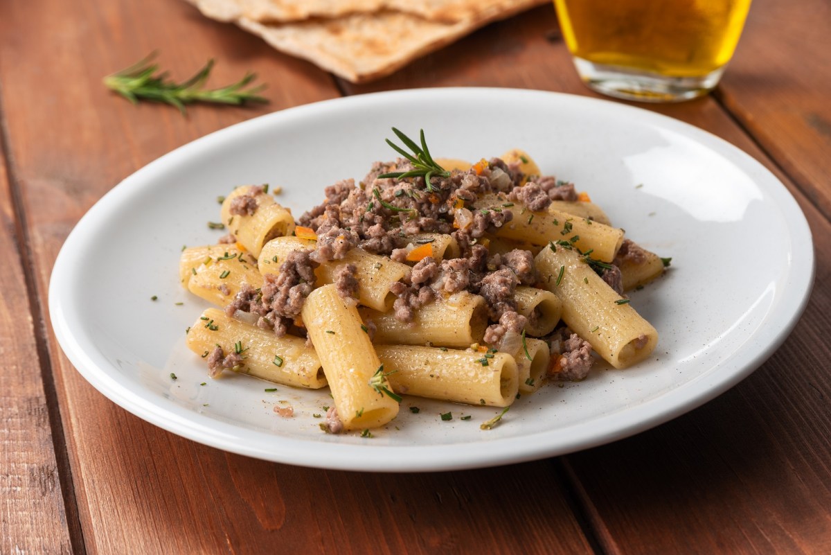 Rigatoni mit weiÃŸer Bolognese auf einem weiÃŸen Teller. Die Nudeln sind mit KrÃ¤utern dekoriert.