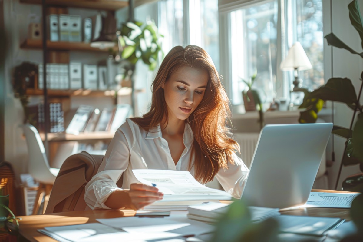 Eine Frau hÃ¤lt ein Dokument in der Hand. Vor ihr steht ein Laptop.