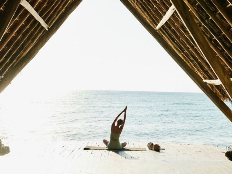 Frau sitzt am Strand und macht Yoga