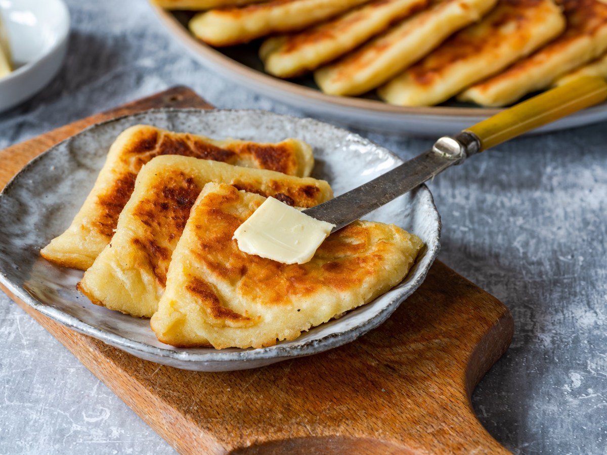 Tattie Scones, serviert mit Butter, auf einem grauen Teller. Im Hintergrund stehen weitere Tattie Scones.