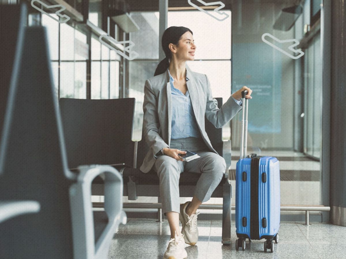 Eine junge Frau sitzt am Gate. Sie hÃ¤lt einen blauen Koffer in ihrer Hand.