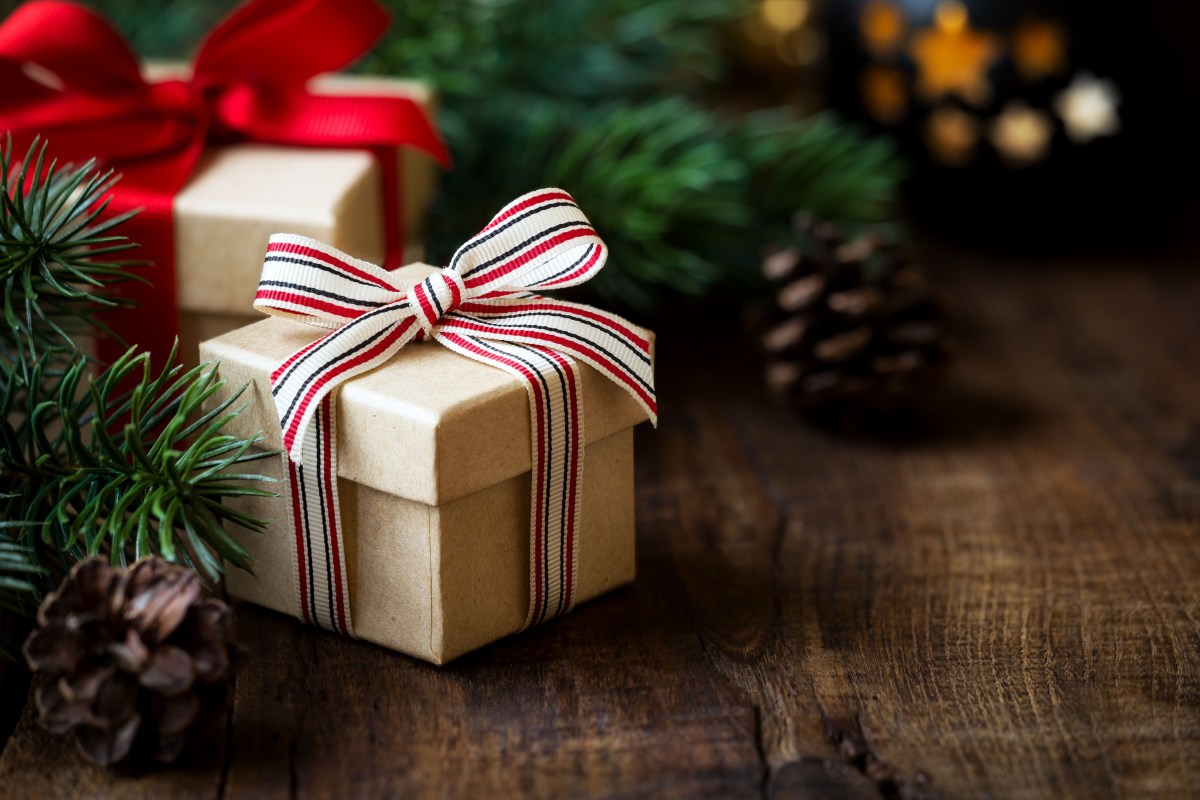 Weihnachtsgeschenk auf einem dunklen rustikalen Holztisch mit Tannenzapfen und Tannenzweigen.