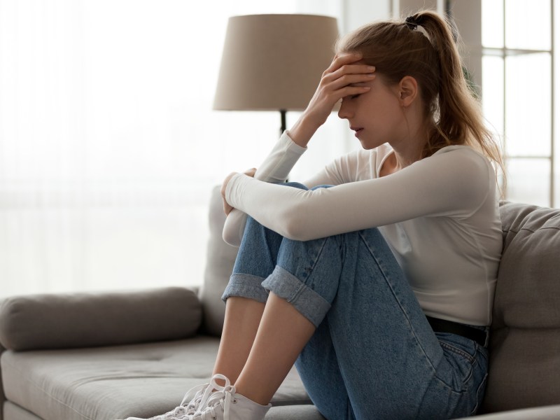 Verzweifelte sitzt auf der Couch, umarmt die Knie, bedeckt ihr Gesicht mit der Hand.