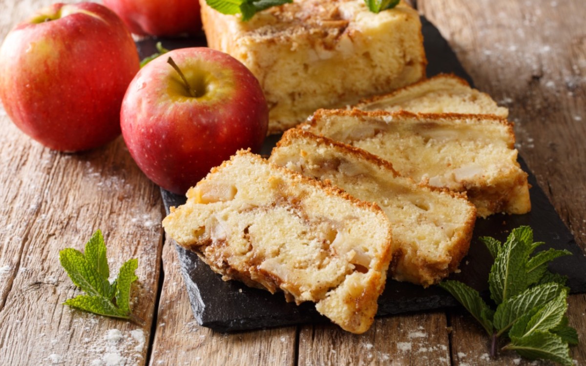 Mehrere StÃ¼cke Apfelbrot, die gefÃ¤chert vor dem restlichen Kuchen liegen. Daneben zwei Ã„pfel.