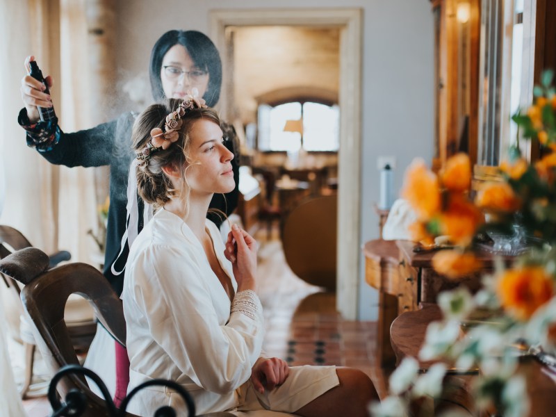 Eine junge Frau macht einer Frau die Haare. Sie versprÃ¼ht Haarspray. Ausbildung Jobs