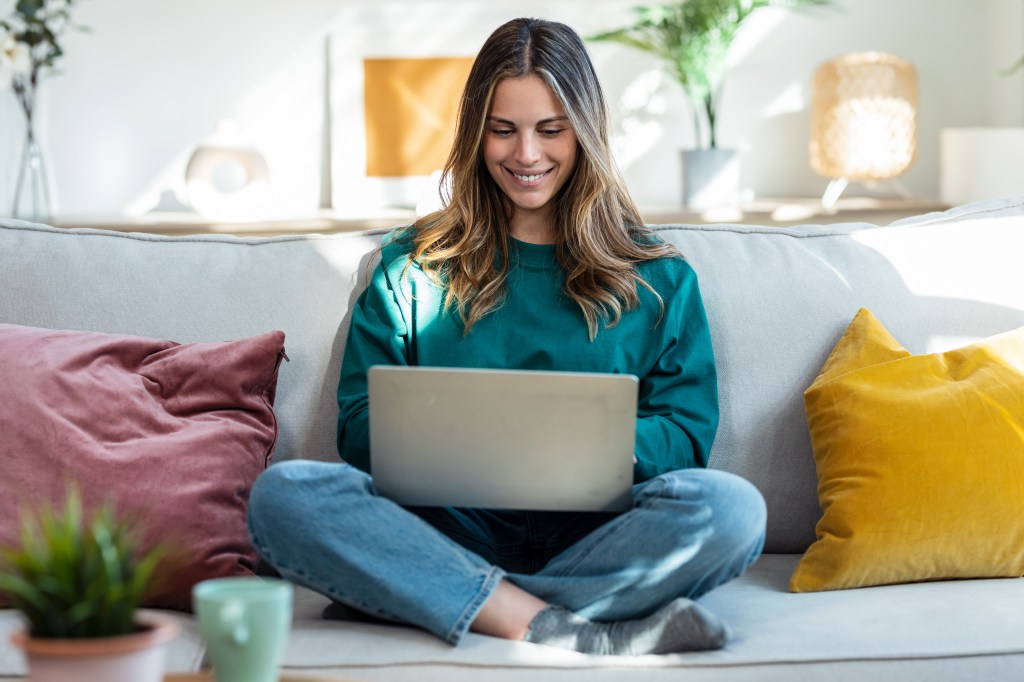 Frau sitzt auf dem Sofa und arbeitet am Laptop.