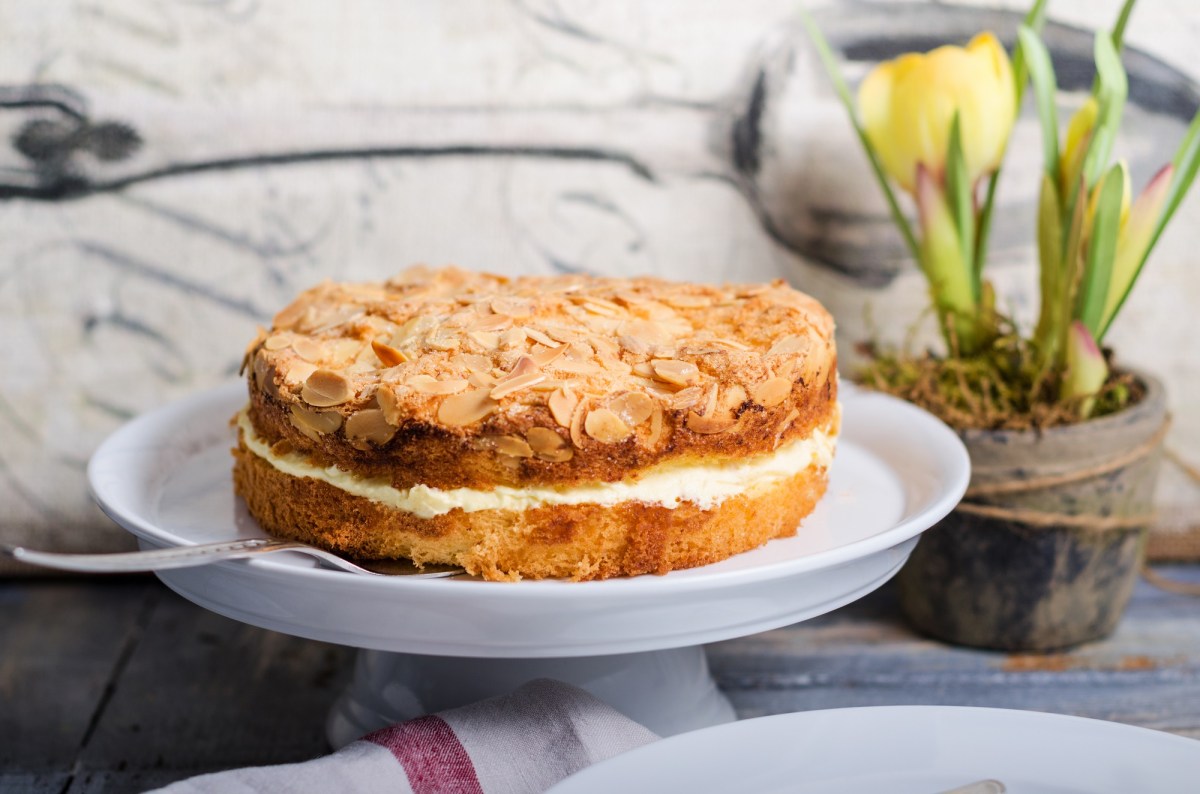 Ein Bienenstich-Kuchen auf einer Tortenplanne, daneben frische Tulpen.