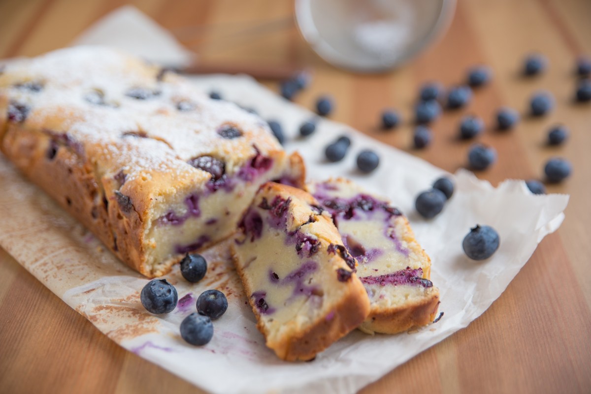 Blaubeer-Joghurt-Kuchen auf Backpapier mit zwei abgeschnittenen StÃ¼ckchen.