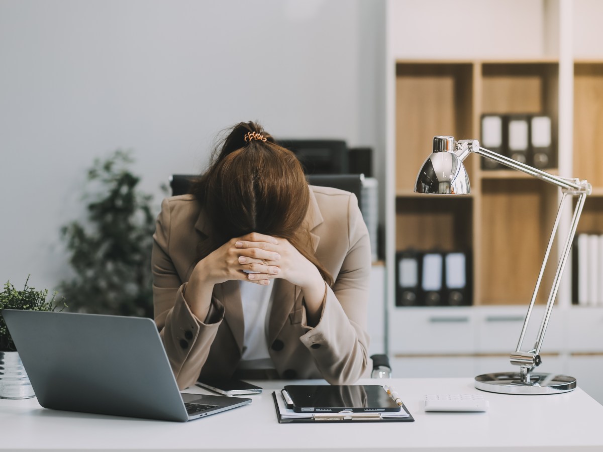 Eine junge Frau sitzt im BÃ¼ro und ist erschÃ¶pft. Sie legt den Kopf auf ihre HÃ¤nde.