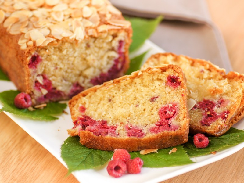 Ein angeschnittener Himbeer-Mandel-Kuchen auf einem Tisch.