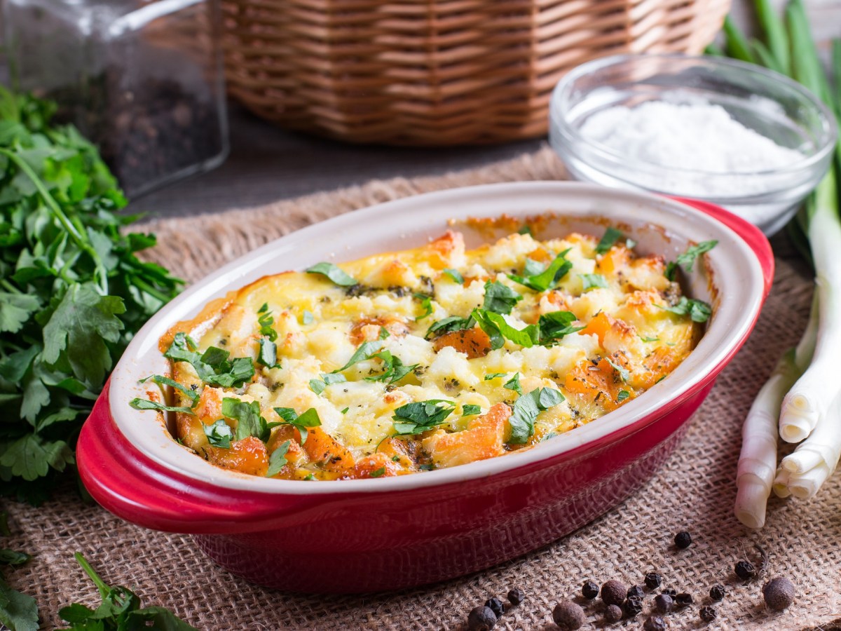 KÃ¼rbis-Gnocchi-Auflauf in ovaler, roter Auflaufform, daneben einige frische Zutaten.