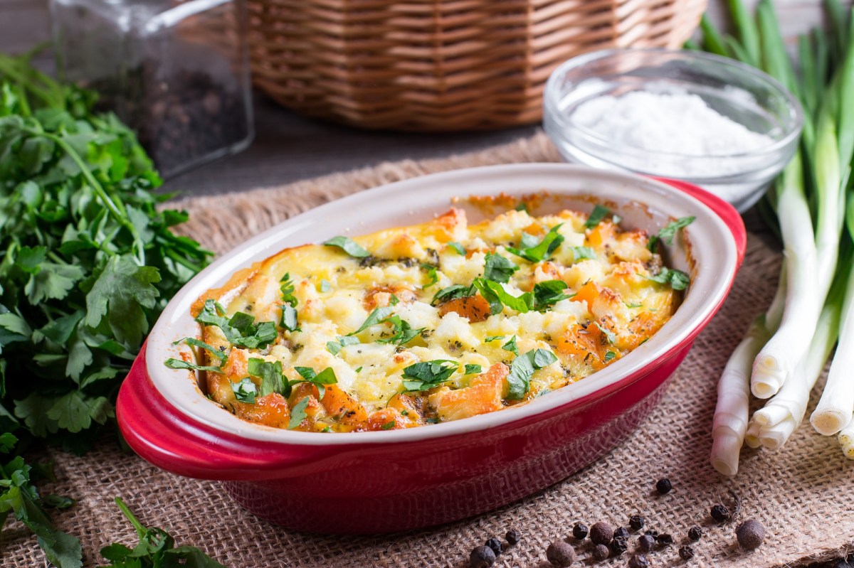 KÃ¼rbis-Gnocchi-Auflauf in ovaler, roter Auflaufform, daneben einige frische Zutaten.