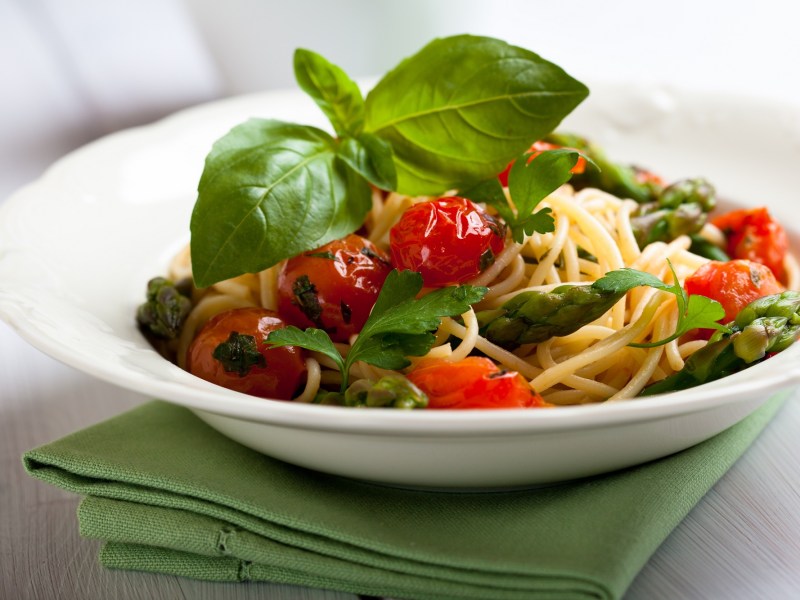 Teller mit Spaghetti mit geschmolzenen Tomaten und grÃ¼nem Spargel.