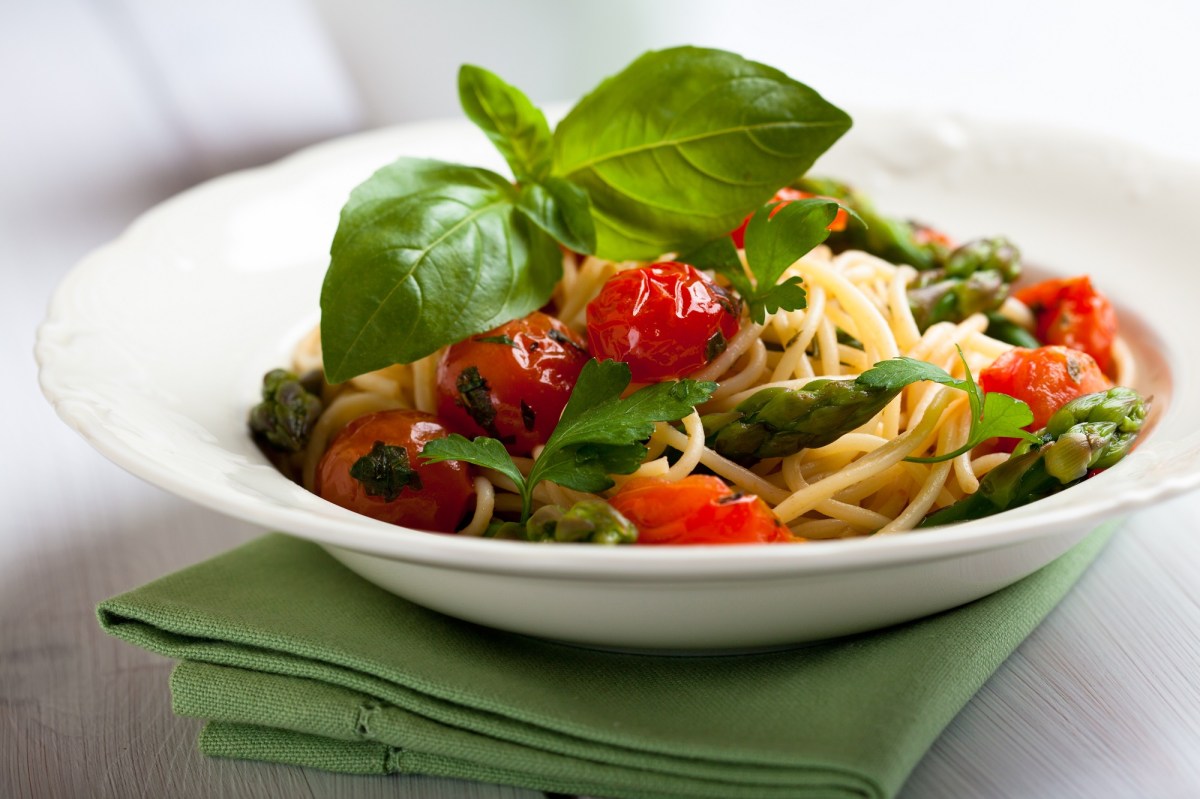 Teller mit Spaghetti mit geschmolzenen Tomaten und grÃ¼nem Spargel.