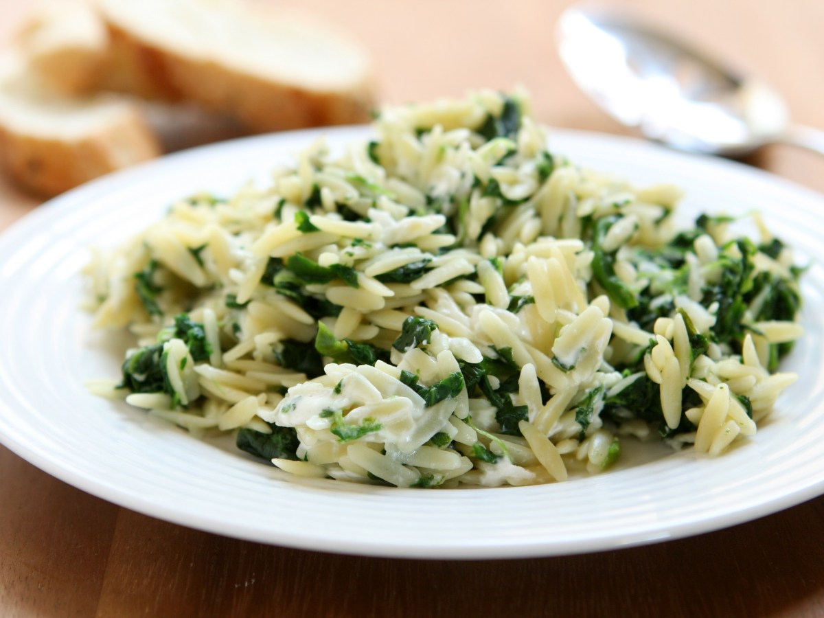 Ein Teller Orzo-Nudeln mit Spinat und Feta, daneben ein LÃ¶ffel und Baguettescheiben.