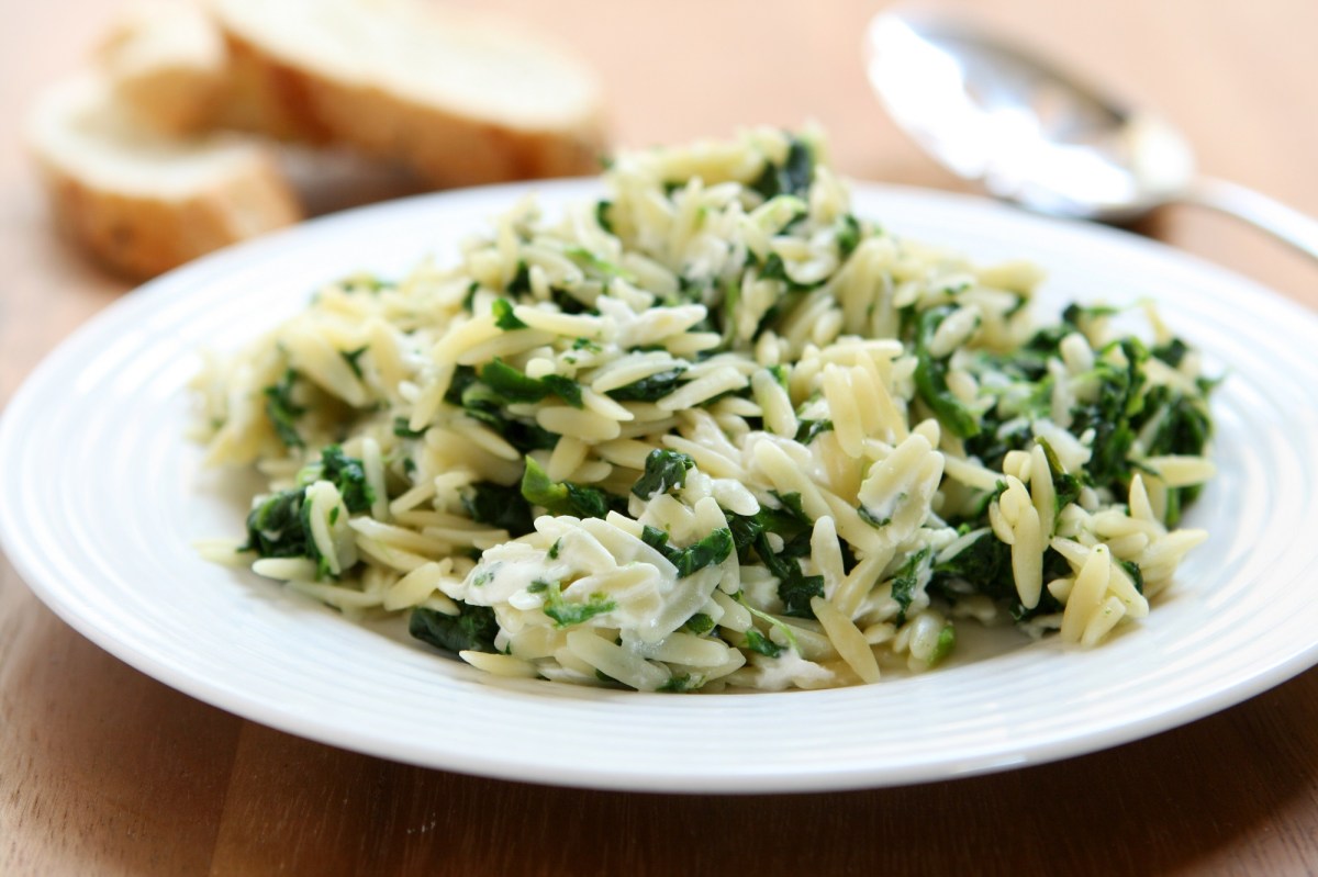 Ein Teller Orzo-Nudeln mit Spinat und Feta, daneben ein LÃ¶ffel und Baguettescheiben.